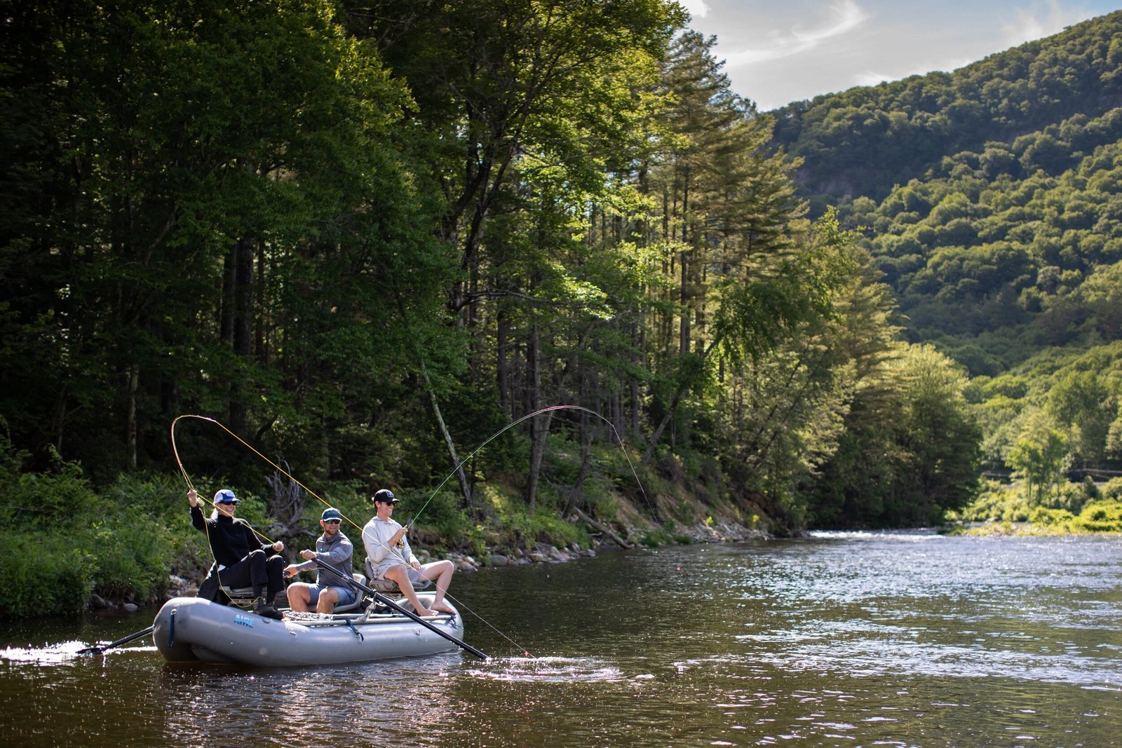 A raft of anglers casting beneath a forested cliff