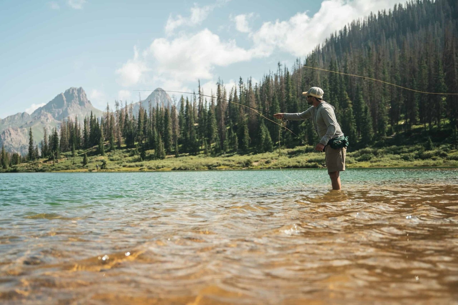 An angler casting into an alpine lake ringed by peaks