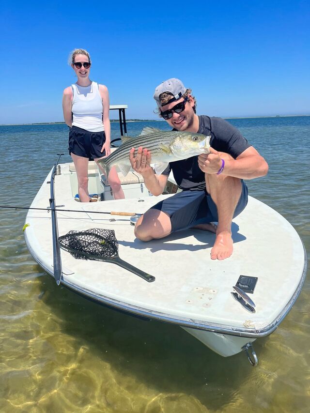 Two clients on a flats skiff with a striped bass