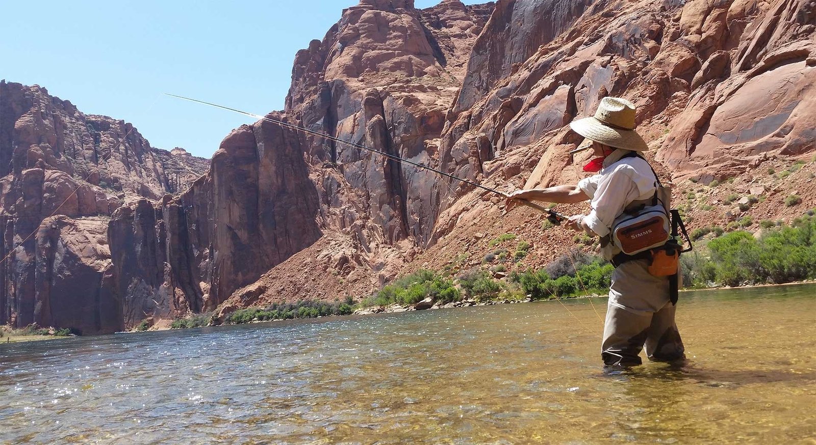 An angler casting beneath towering red canyon walls