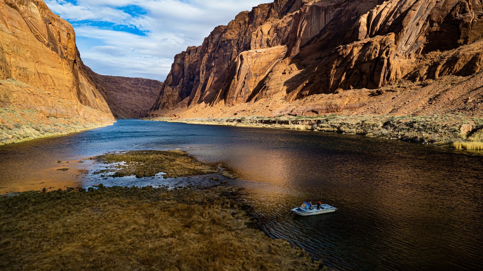 A fishing boat on a wide desert canyon river at golden hour