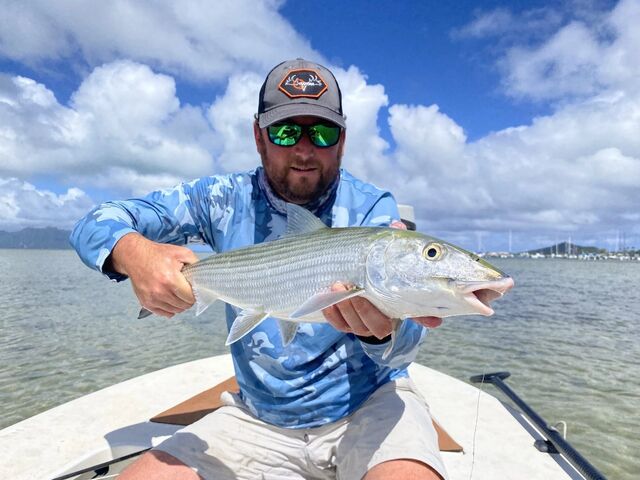 An angler holding a bonefish on a bright saltwater flat