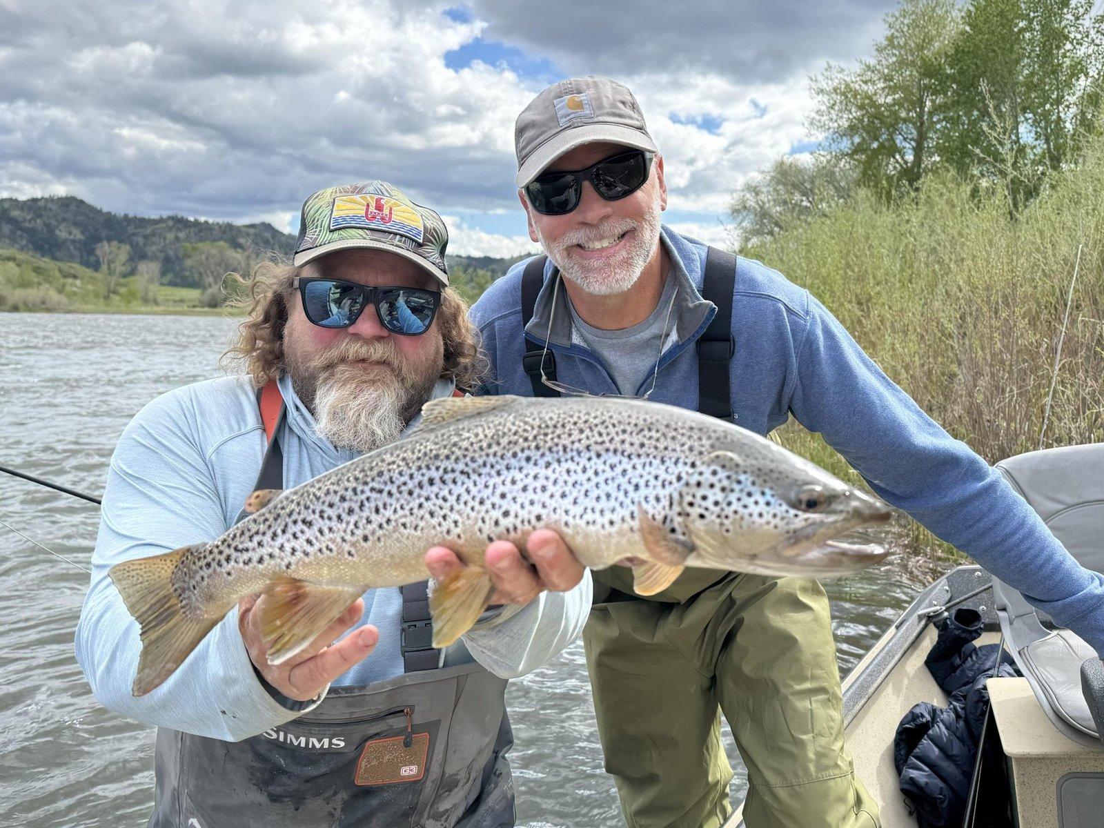 A guide and angler grinning over a heavy brown trout at the boat
