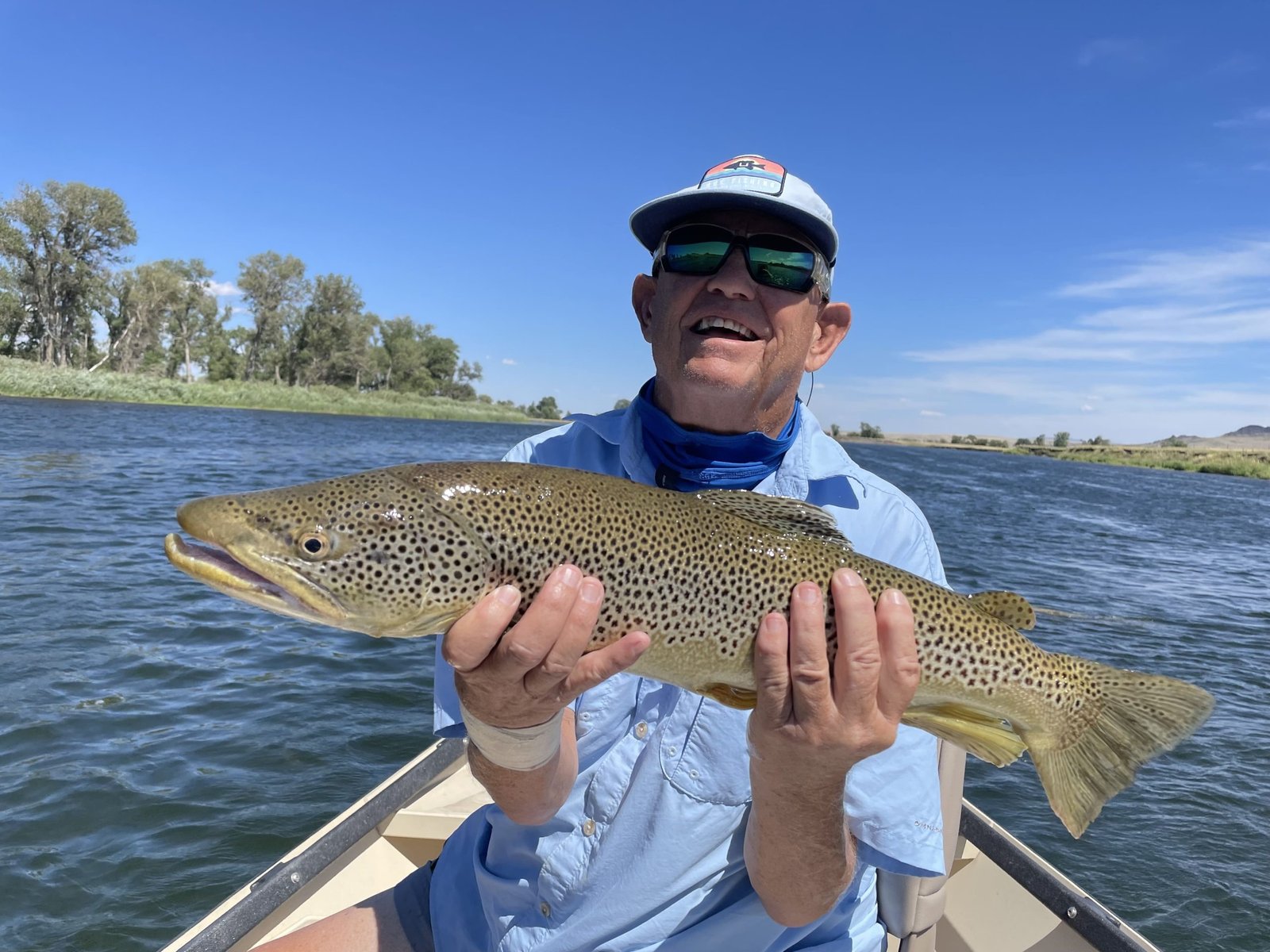 A smiling angler holding a golden brown trout from the drift boat