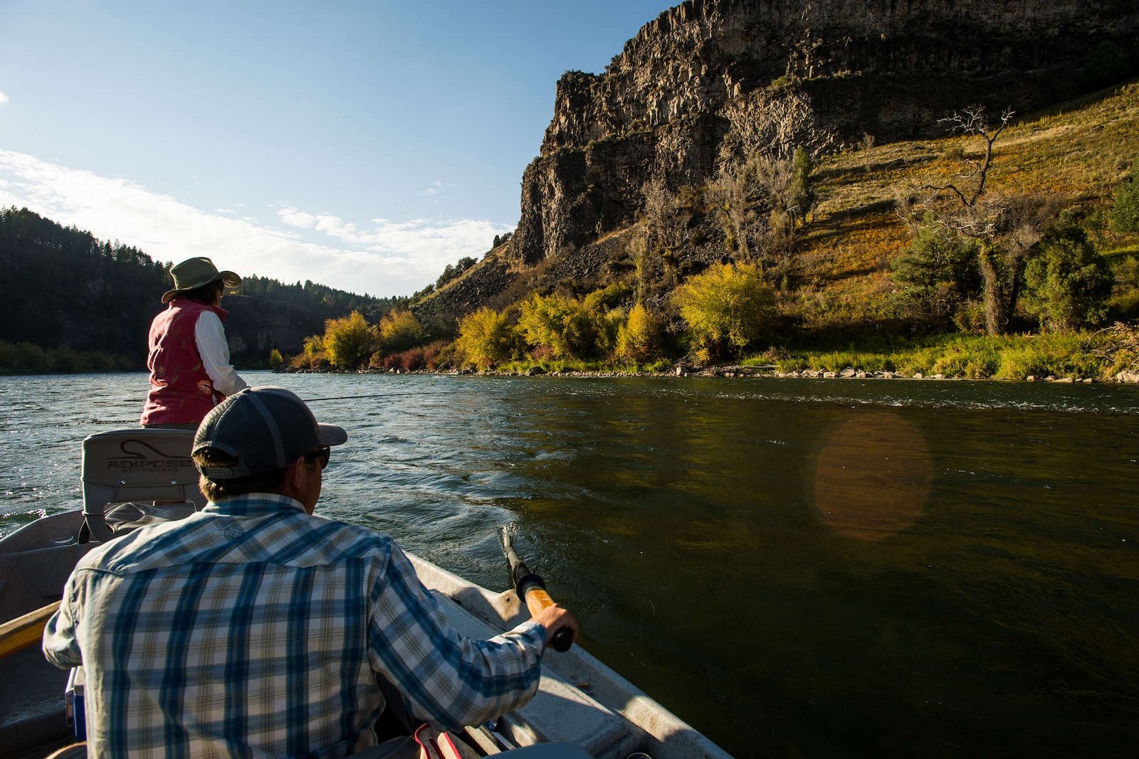 A guide rowing anglers down a canyon river in golden evening light