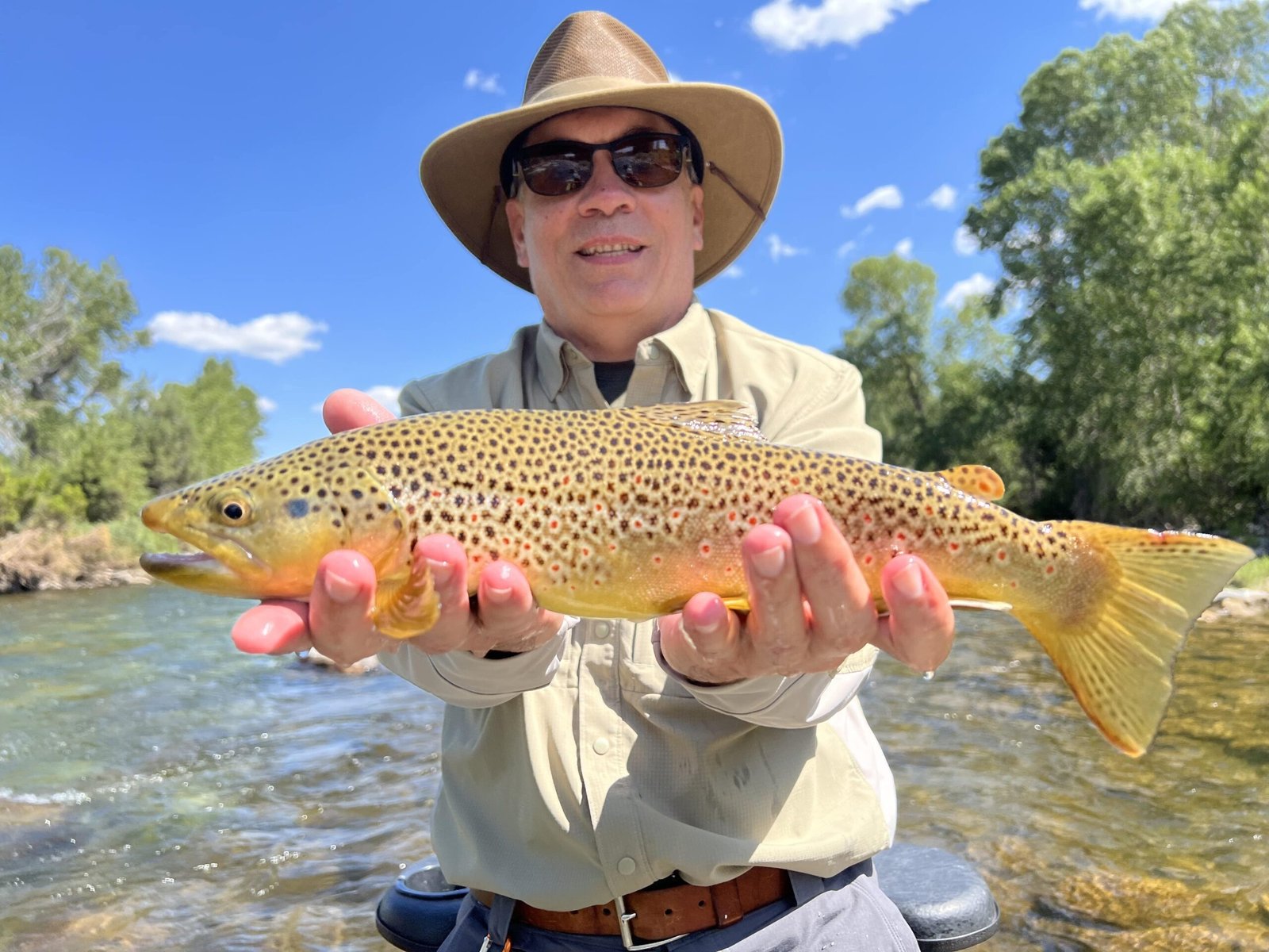 A smiling angler in a sun hat holding a golden brown trout