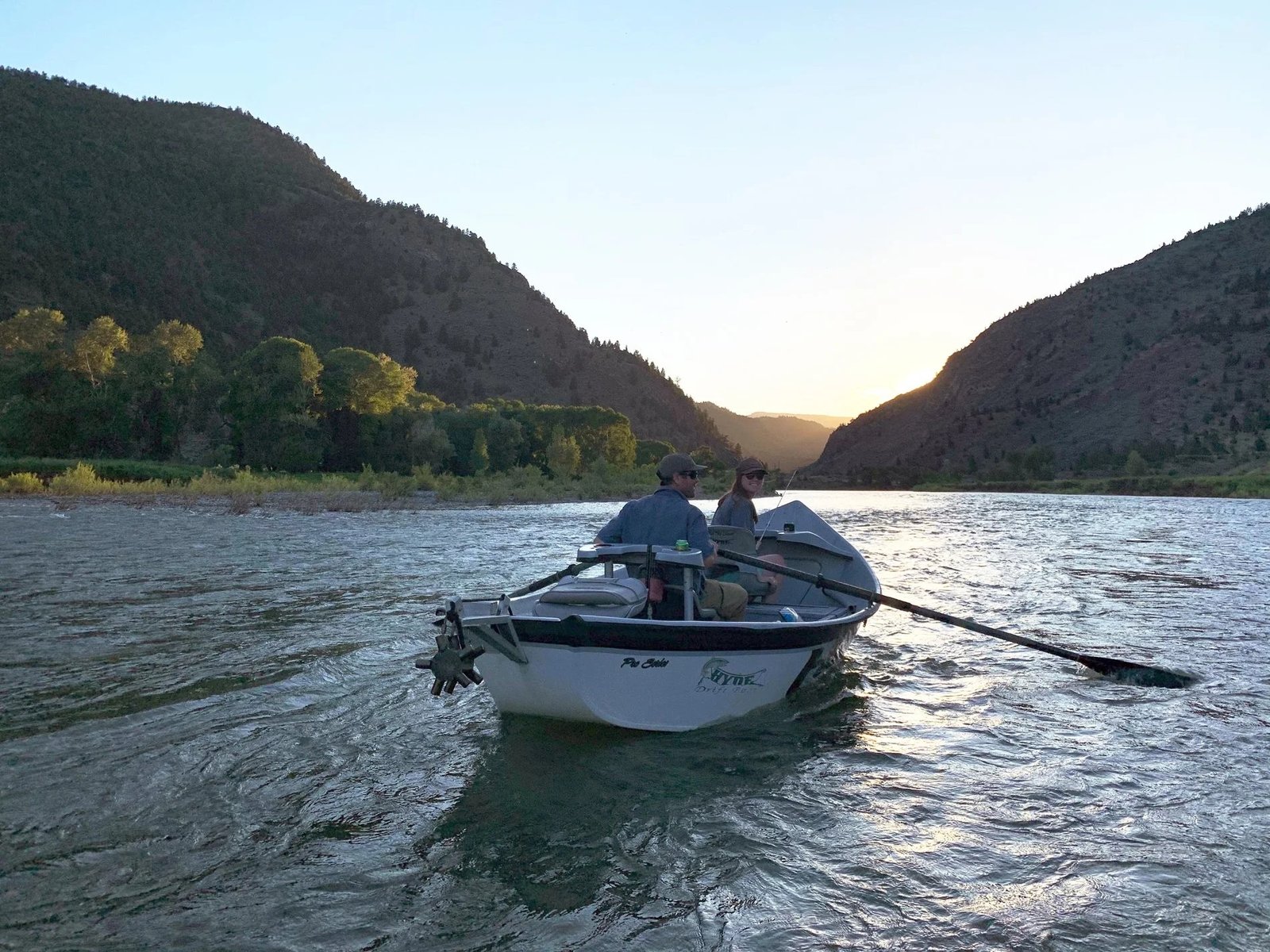 A drift boat rowing downriver into the evening light